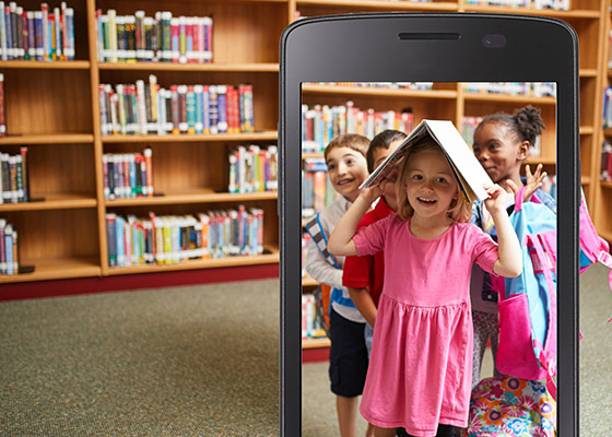 Image on phone of group of children and one of them is holding a yearbook on their head