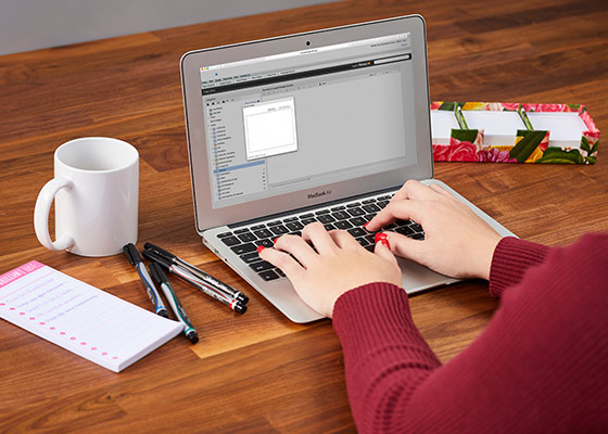 person on computer uploading image to the website with coffee and pens on the table