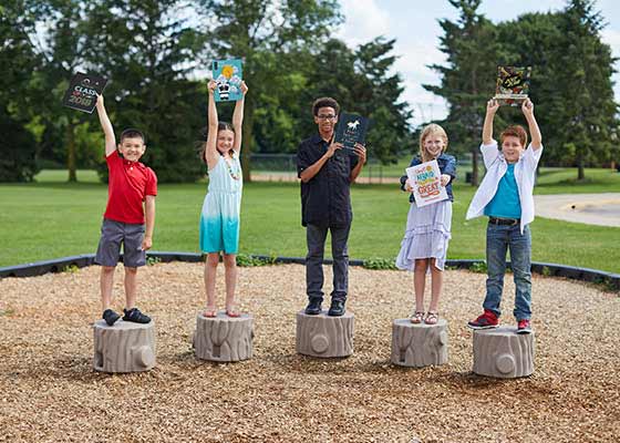 five children on a playground holding up yearbooks