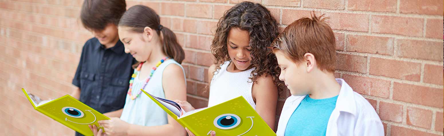 four children leaning on a brick wall looking at two yearbooks